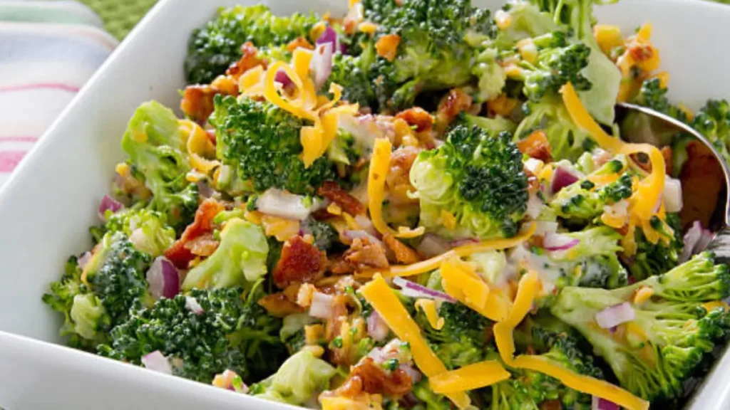 a vibrant Broccoli Salad with Coleslaw Dressing with crispy bacon bits, shredded cheddar cheese, and chopped red onions, all mixed with a creamy dressing.