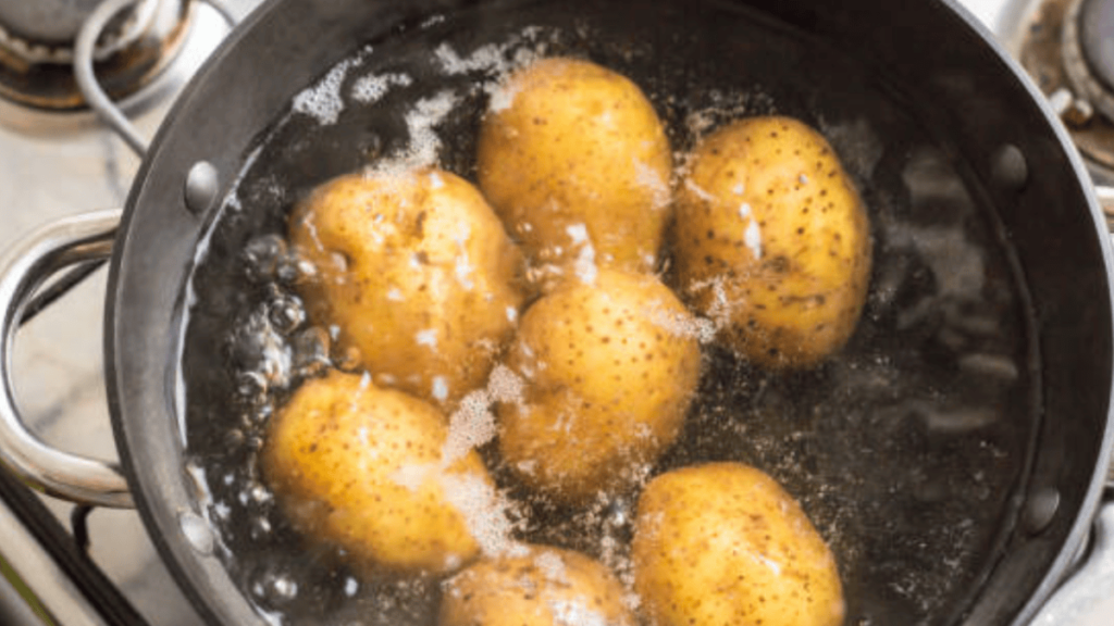a pot of who leInstant Pot Baked Potatoes being boiled in water on a stovetop. The potatoes have their skins on and are submerged in bubbling water.
