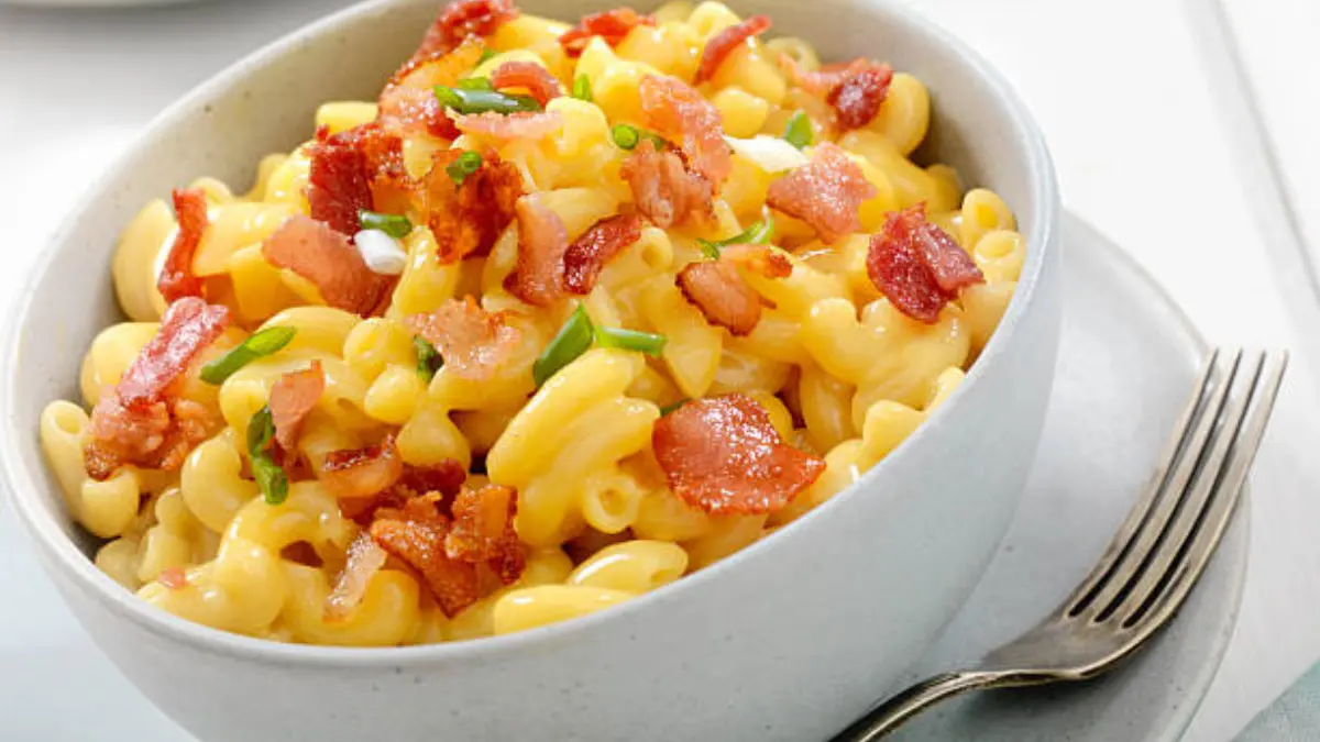 a bowl of creamy Macaroni and cheese cups topped with crispy bacon bits and chopped green onions. The golden, gooey cheese coats the elbow pasta, creating a rich and comforting dish