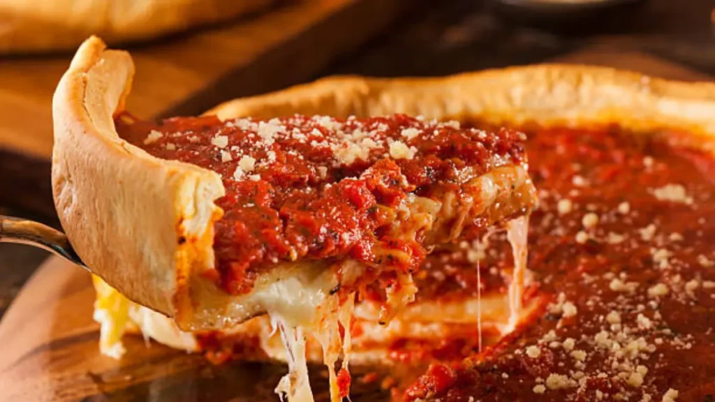 showcases a delicious slice of Chicago-style deep-dish Stuffed pizzabeing lifted from the pan. The pizza has a thick, golden crust filled with layers of gooey, melted cheese and savory toppings, all topped with a rich, chunky tomato sauce